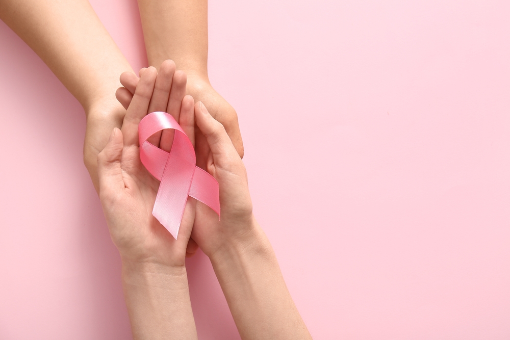 Women holding pink ribbon on color background, closeup. Breast cancer awareness concept
