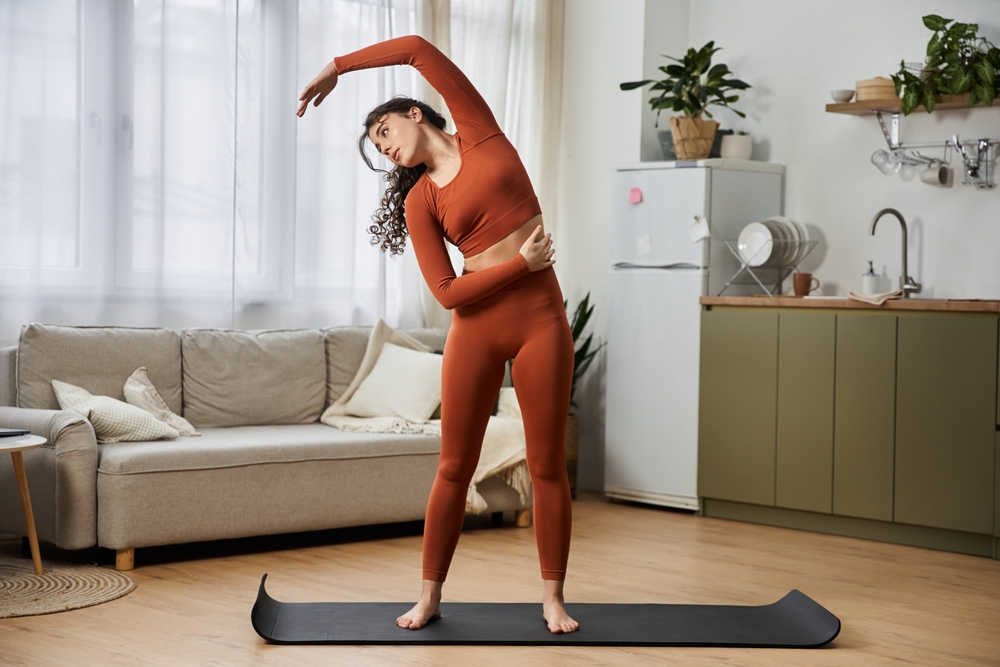 A beautiful young woman performs a gentle stretch at home, embracing the calm of the morning light.