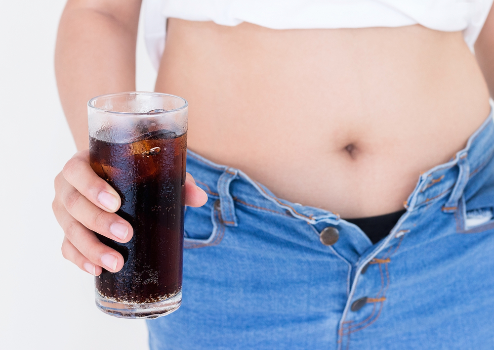 Woman holding glass of cola with Jeans too tight on belly fat and paunch, Diet concept, Weight lose concept.
