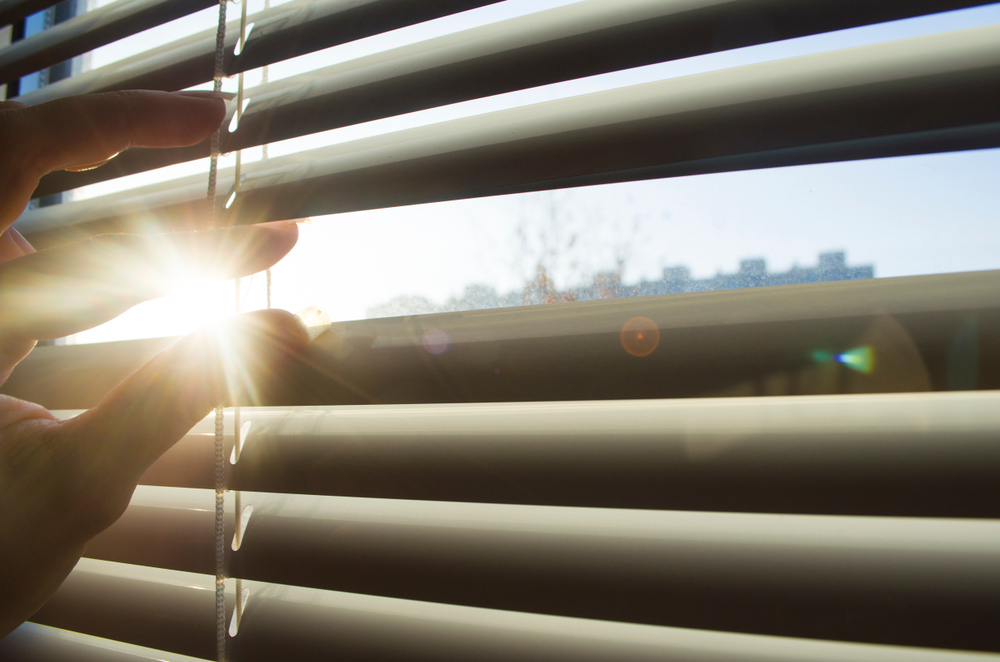 hand opens the blinds or jalousie in sunny day. sunlight rays. sun beam