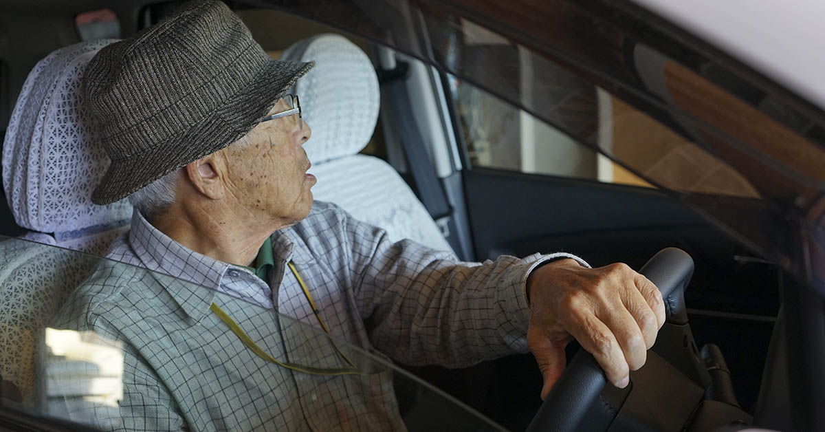 Elderly man in drivers seat of car, looking out the window. Seniors driving concept