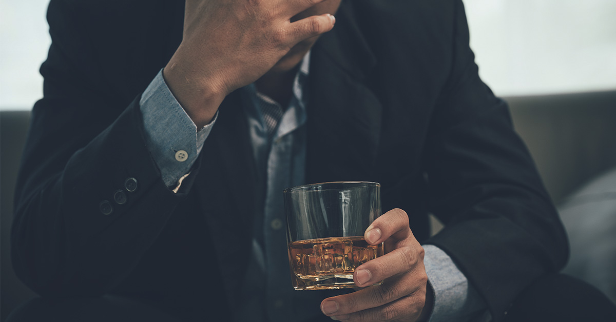 Man holding a glass with amber coloured alcohol. Binge drinking concept