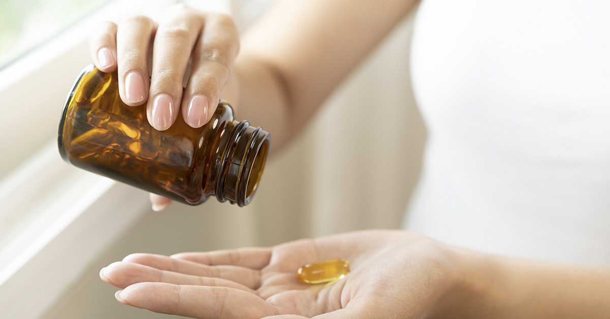 woman dispensing supplements into palm of her hand from a brown glass jar