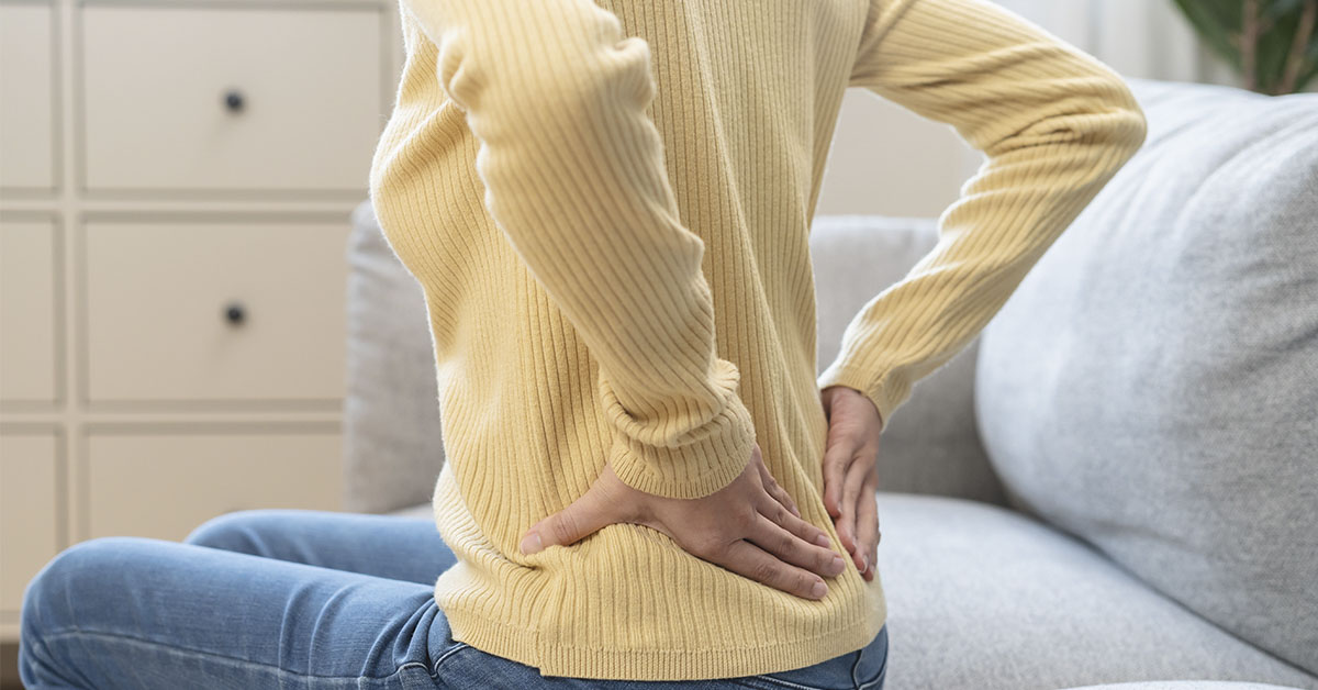 woman holding her lower back while sitting on a ouch. Low back pain concept