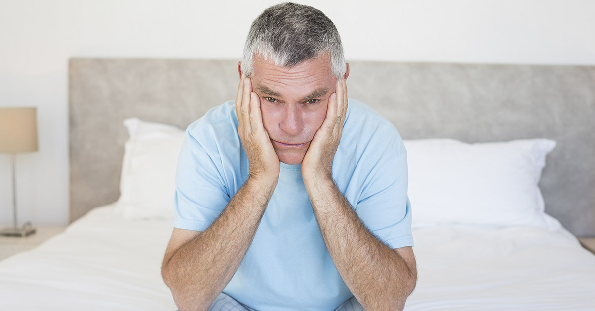 Sad middle aged man sitting on end of bed