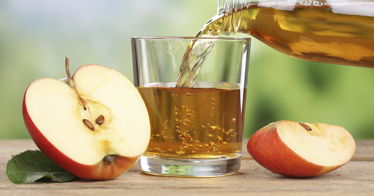 Apple Juice being poured into a glass. Sliced apples placed beside glass.