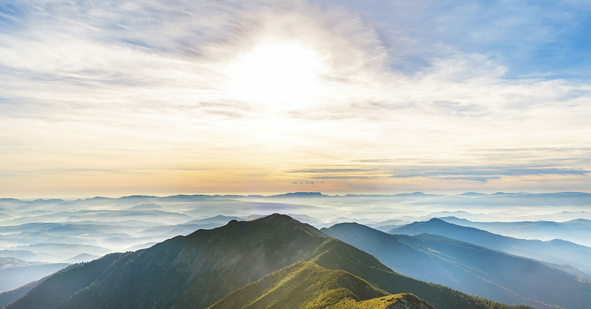 mountain ranges above the clouds with sun setting in background