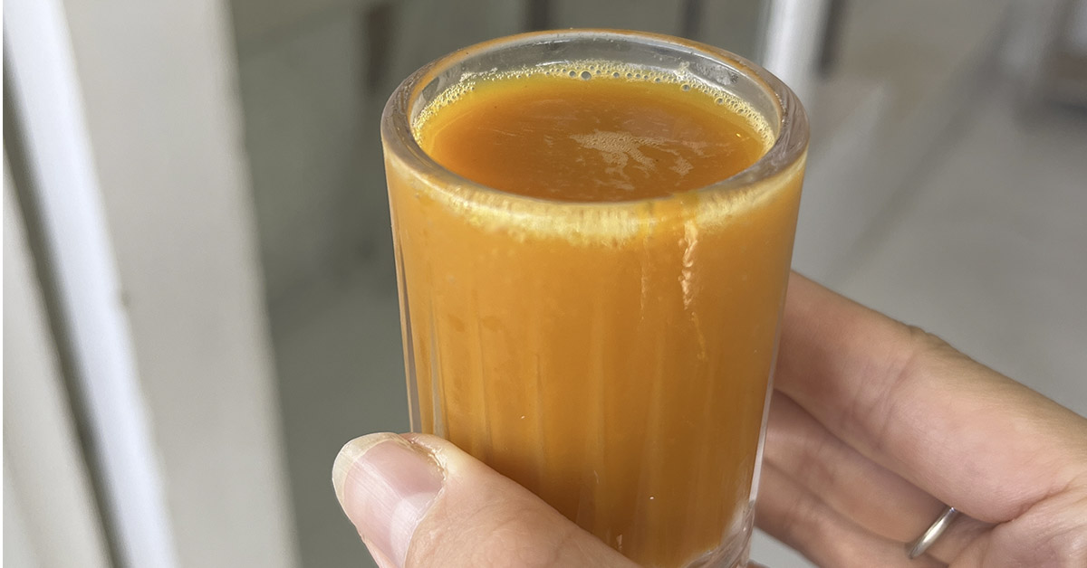 person holding a Turmeric-Ginger Shot in a small glass