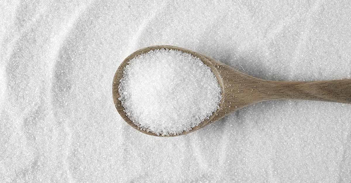 wooden spoon filled with table sugar, sitting on bed of table sugar