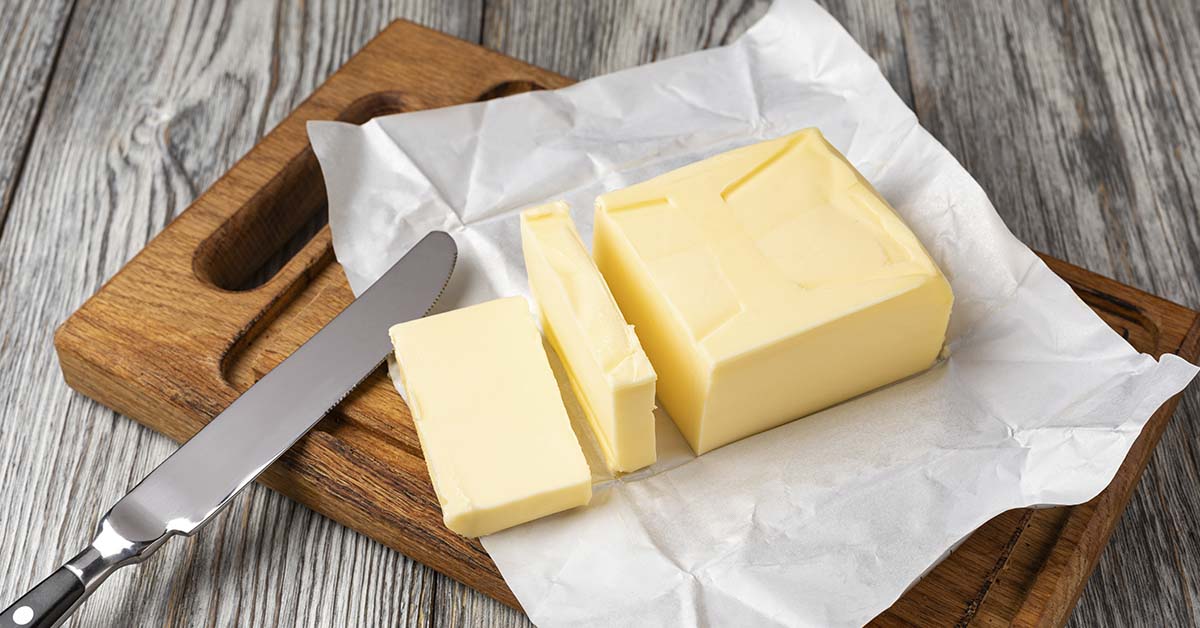 stick of butter unwrapped on cutting board with butter knife