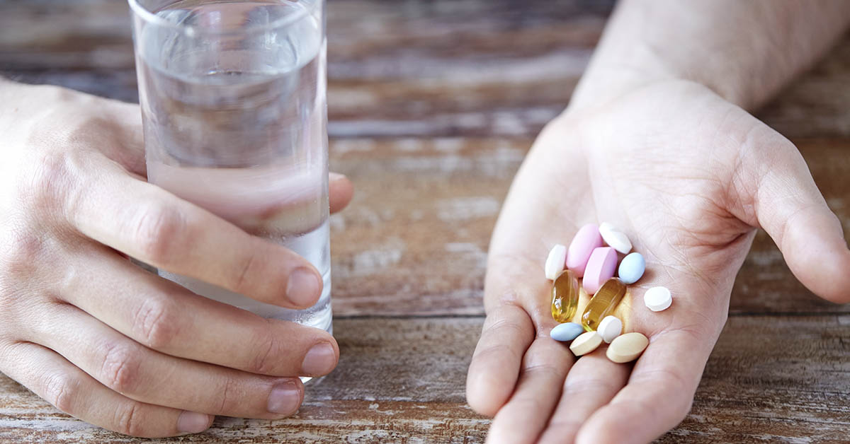 person holding a glass of water in one hand and pills and supplements in the other
