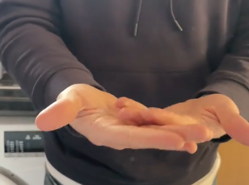 The Tiktoker's boyfriend in a dark hoodie holds both hands out in front of them, palms cupped and facing up. The text “Brain tumour awareness” appears above their hands, introducing a simple coordination test highlighted in the article.