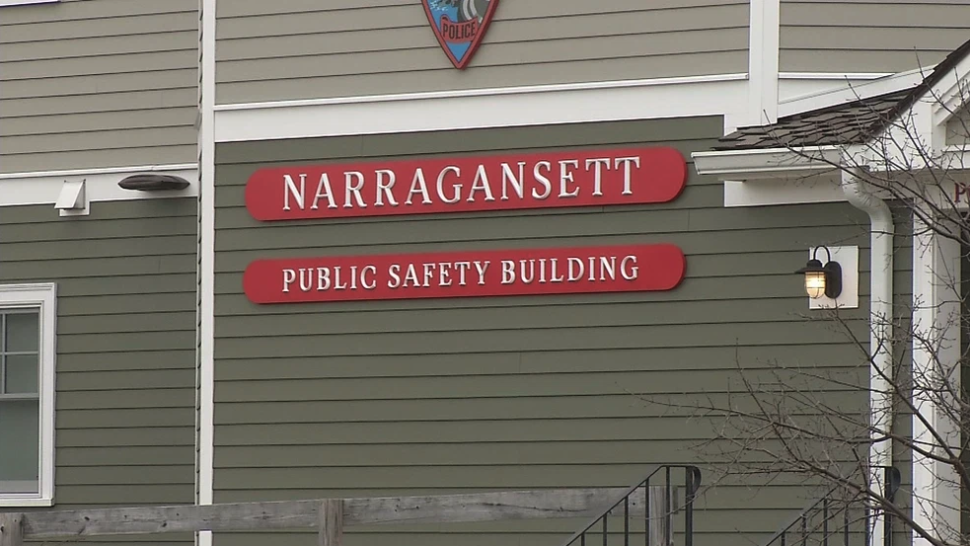 Narragansett Public Safety Building with red identification signs mounted on gray siding. Police from this department conducted a fruitless beach search with cadaver dogs after an anonymous social media post claimed bodies were buried there, later revealed to be part of someone's fictional writing project.