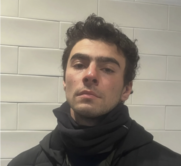 Luigi Mangione in black hoodie against white tile wall, the 26-year-old who shot Thompson after experiencing his own frustrations with health insurance coverage.