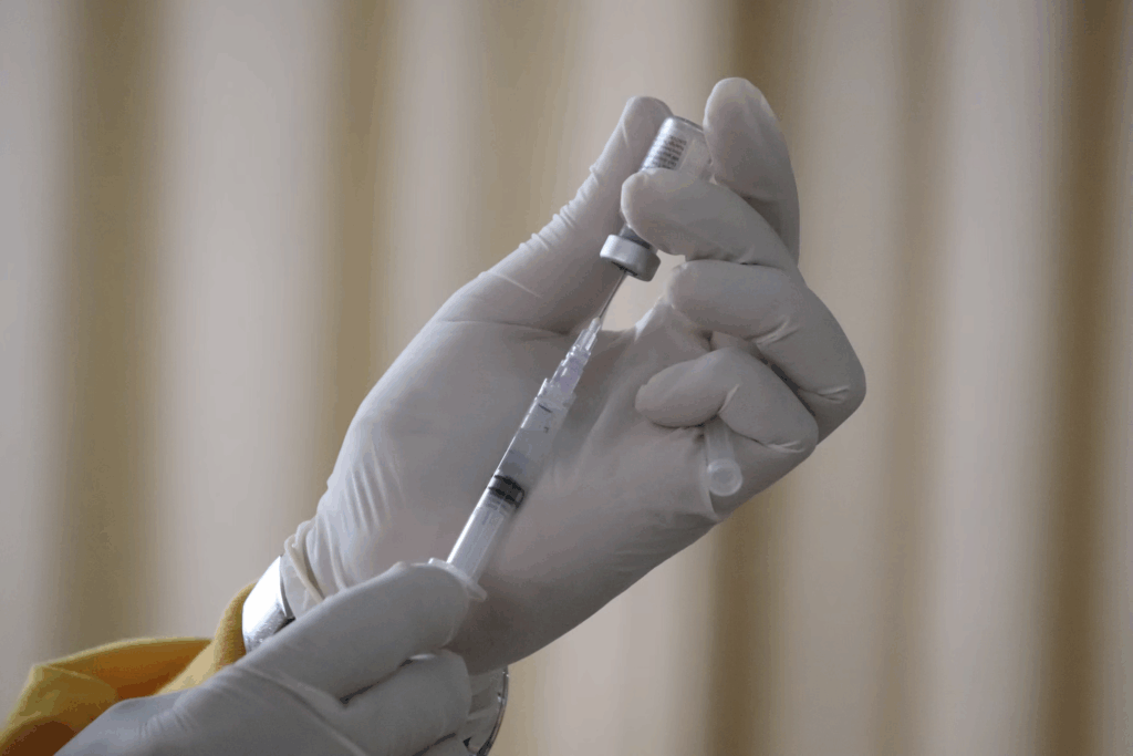 A healthcare professional's gloved hand holding a prepared syringe for injection. This new five-minute treatment method helps save NHS staff approximately 1,000 hours of treatment time monthly, creating capacity for more patient appointments without additional cost.