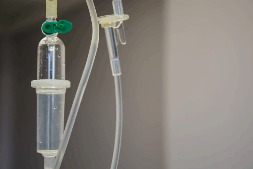An intravenous (IV) drip system showing clear tubing and medication chamber with a green clip. This traditional immunotherapy delivery method requires patients to remain connected to the IV pole for up to an hour, limiting their mobility and extending treatment time.