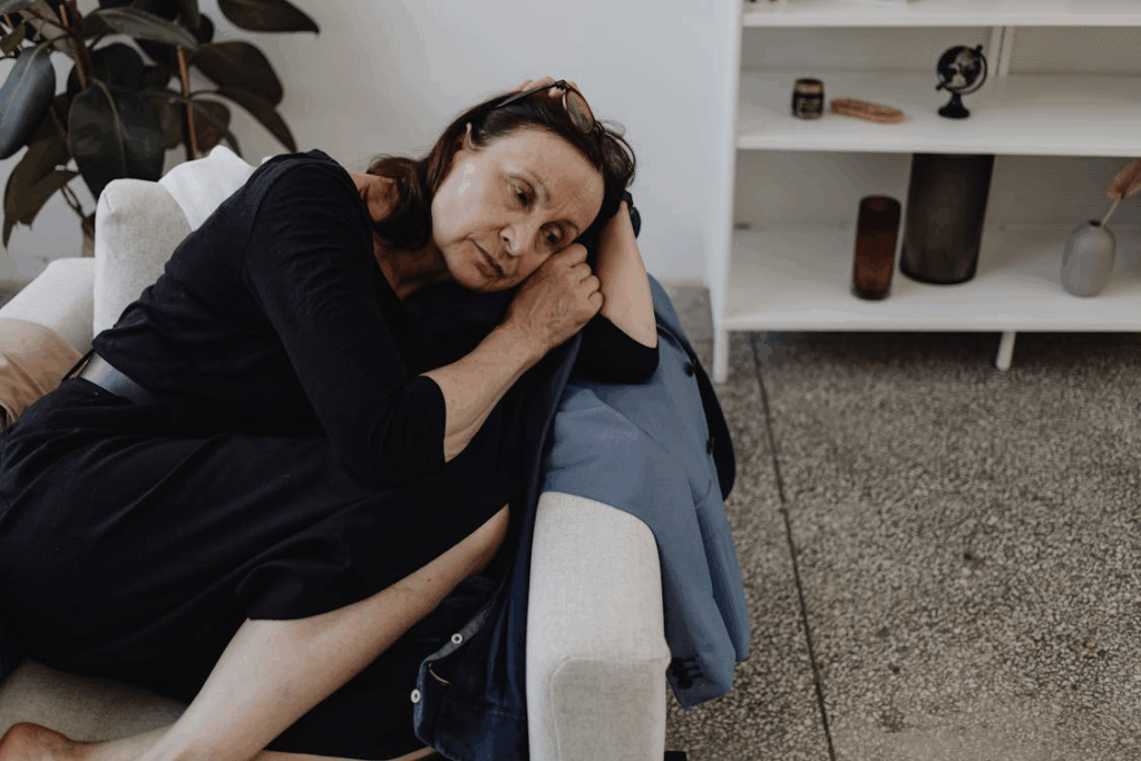 A middle-aged woman in black clothing lies on a couch looking dejected and lonely, illustrating the social isolation that can occur when workplace relationships disappear.