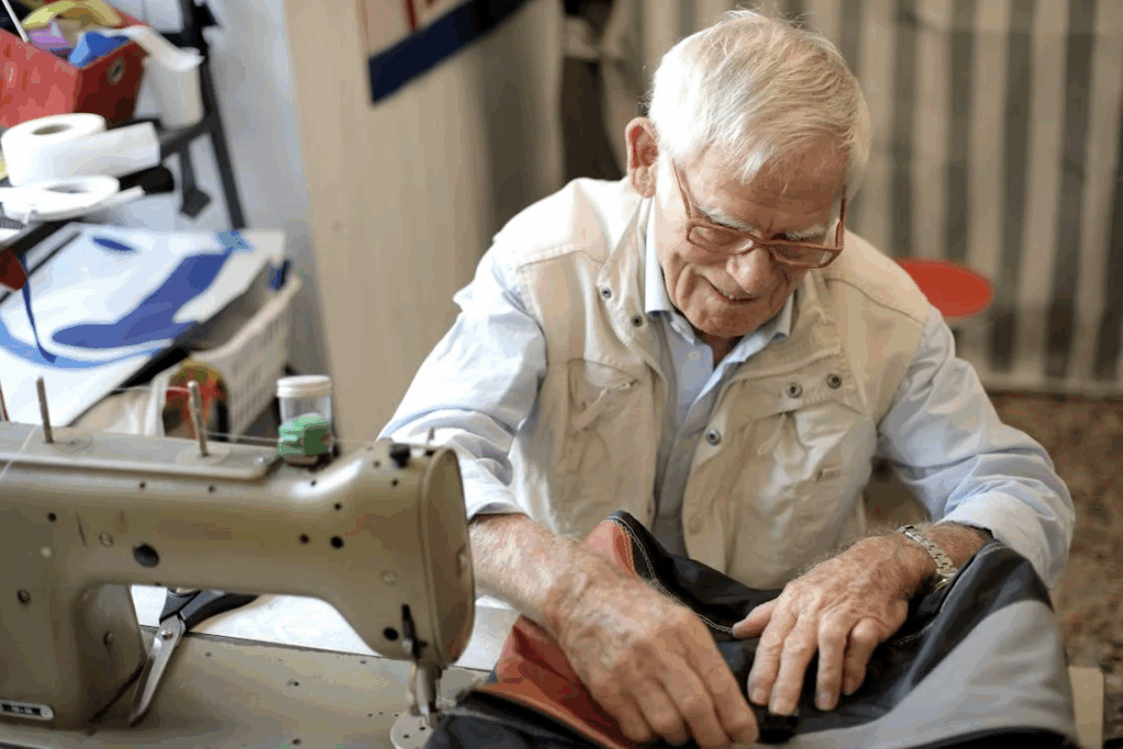 An elderly man with glasses wearing a light-colored shirt works at a sewing machine, showing how volunteering skills during retirement can provide purpose and reduce social disconnection.