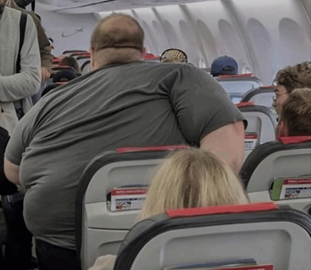 Person with a larger body struggling to fit in a standard airplane seat, showing how cramped air travel can be for plus-sized passengers. The individual's body extends beyond the armrests while seated in what appears to be an economy class cabin.