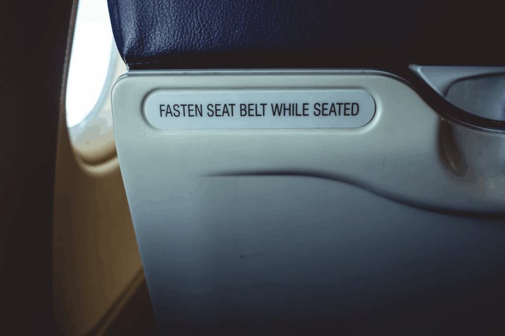 Close-up of an airplane armrest with a safety instruction that reads "FASTEN SEAT BELT WHILE SEATED," highlighting airline policies that affect passenger comfort and safety requirements during flights.