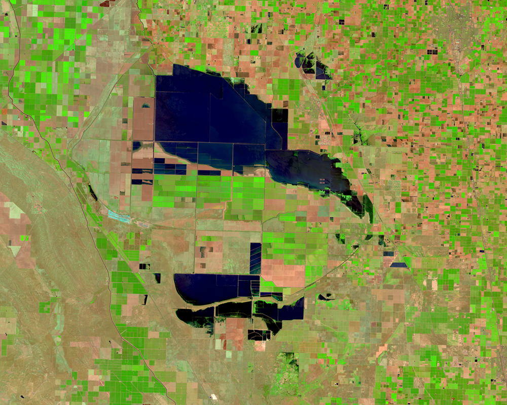Satellite view showing dark blue floodwaters of Tulare Lake covering approximately 180 square miles of California's San Joaquin Valley on April 16, 2023. The geometric patterns of agricultural fields in green, tan and pink surround the unexpected return of this historic body of water, which submerged farms and infrastructure following exceptional winter storms.