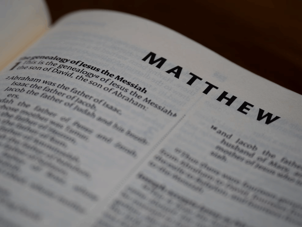 Close-up of an open Bible page showing the beginning of the Gospel of Matthew with visible text stating "The genealogy of Jesus the Messiah" and listing Abraham, Isaac, and Jacob as ancestors. This modern publication contrasts with the ancient Syriac translation recently discovered.