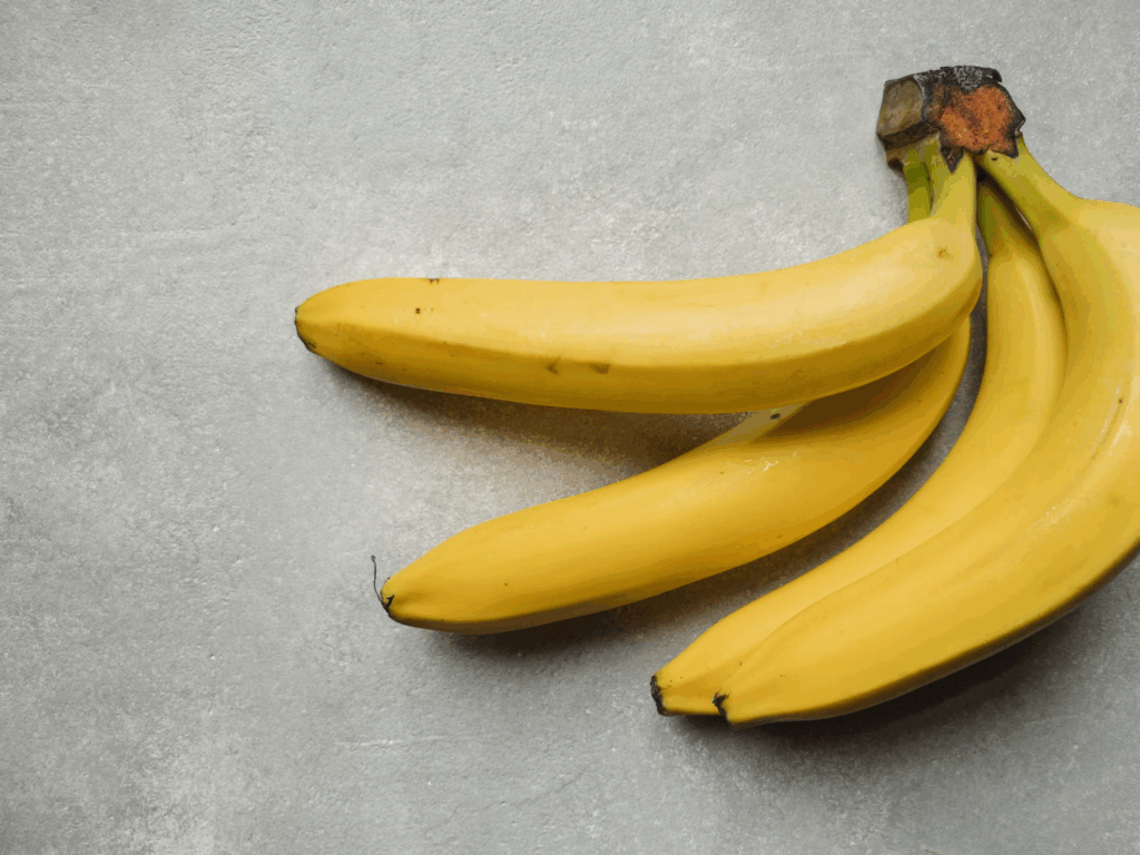 Fresh yellow bananas with brown stem on a gray surface, rich in tryptophan and B vitamins, these mood-boosting foods help create feel-good chemicals in the brain.