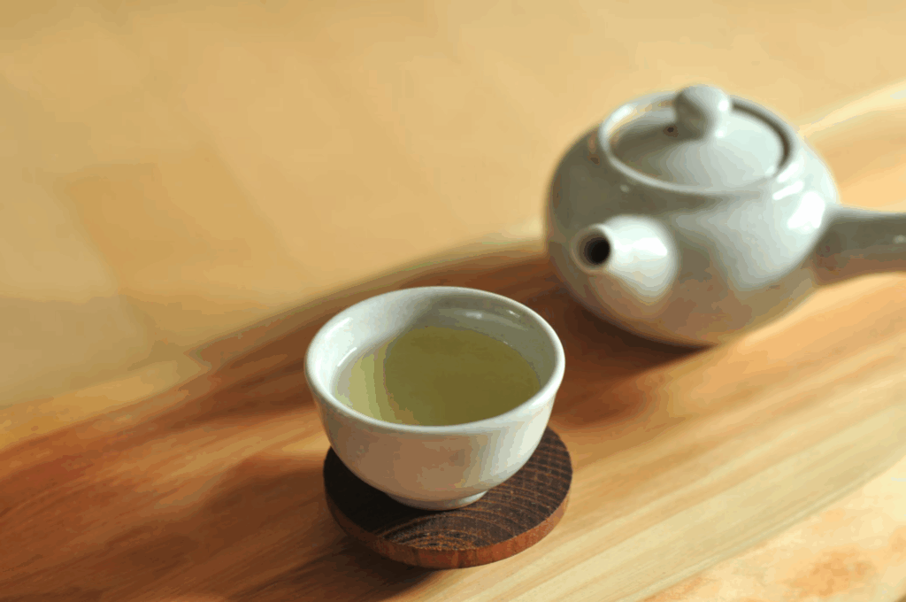 Traditional white teapot and cup with pale green tea on wooden surface, containing L-theanine that creates calming brain waves while keeping the mind alert.