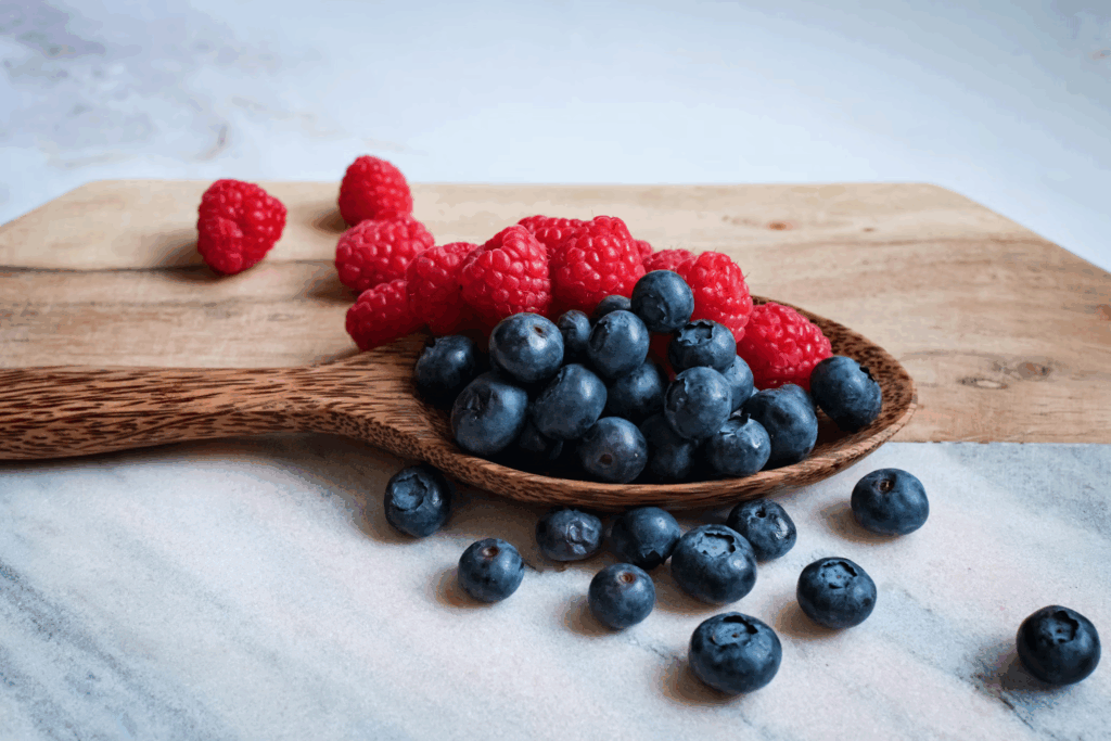 Wooden spoon filled with fresh blueberries and raspberries, colorful mood-boosting foods that fight brain inflammation and balance emotional ups and downs.