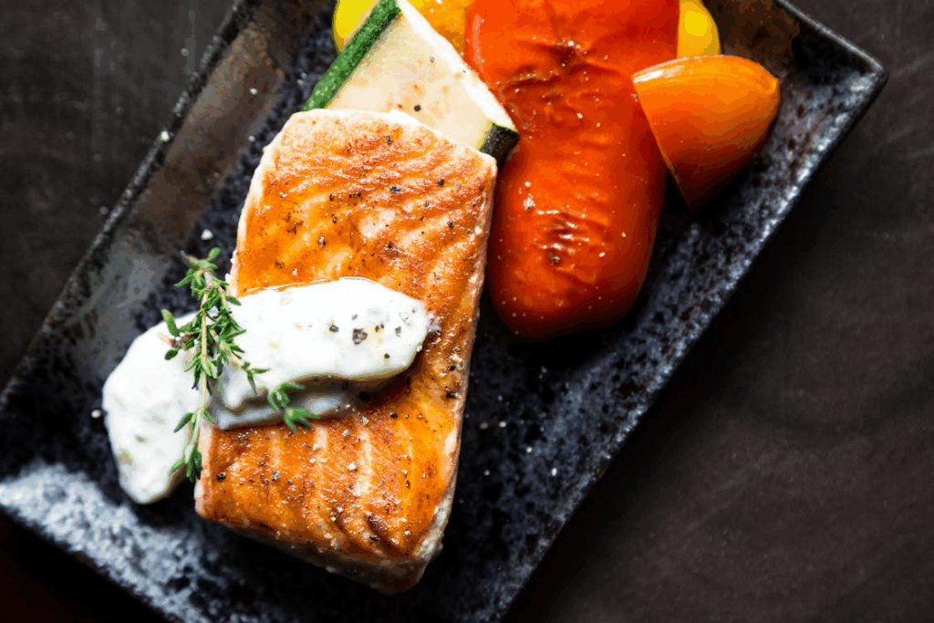 Grilled salmon fillet with sauce and vegetables on black plate, delivering EPA and DHA fats that combat depression and enhance brain cell communication.