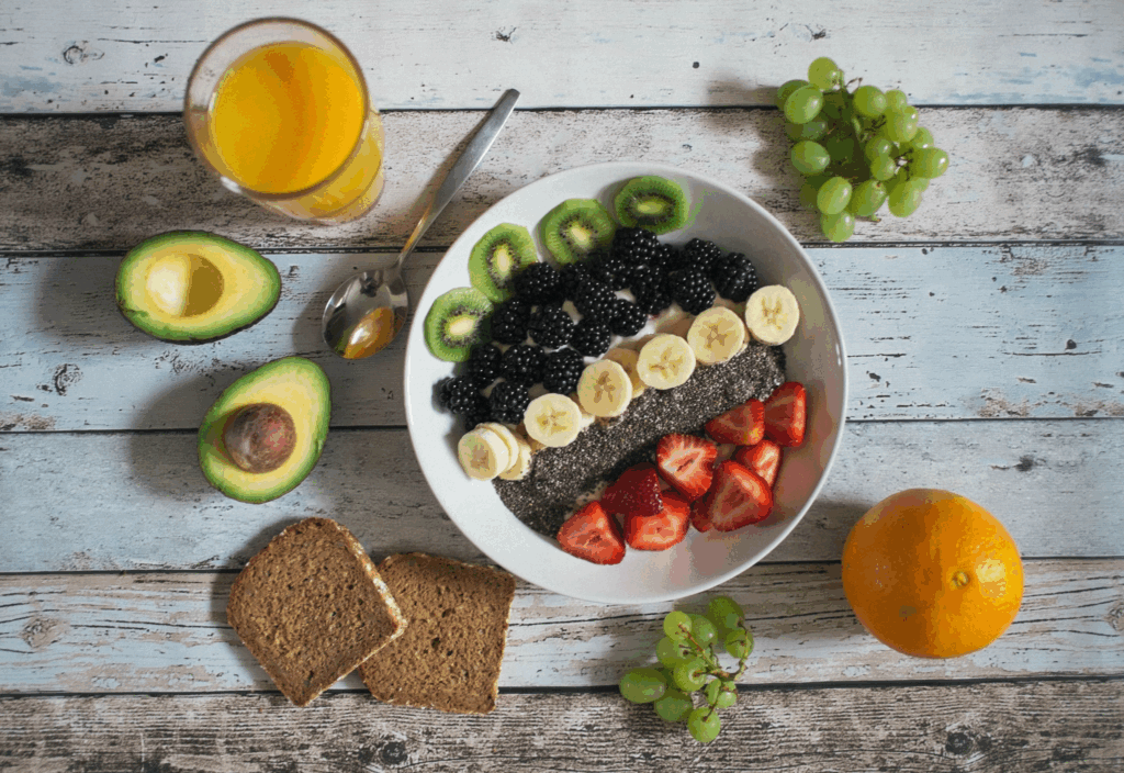 Healthy breakfast bowl with fruits, chia seeds, whole grain toast and avocado on rustic wooden table, showcasing multiple mood-boosting foods in one balanced meal.
