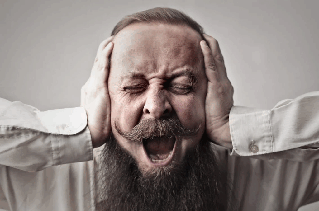 Close-up Photo of Screaming Man With a Full Beard Covering His Ears and Closing His Eyes