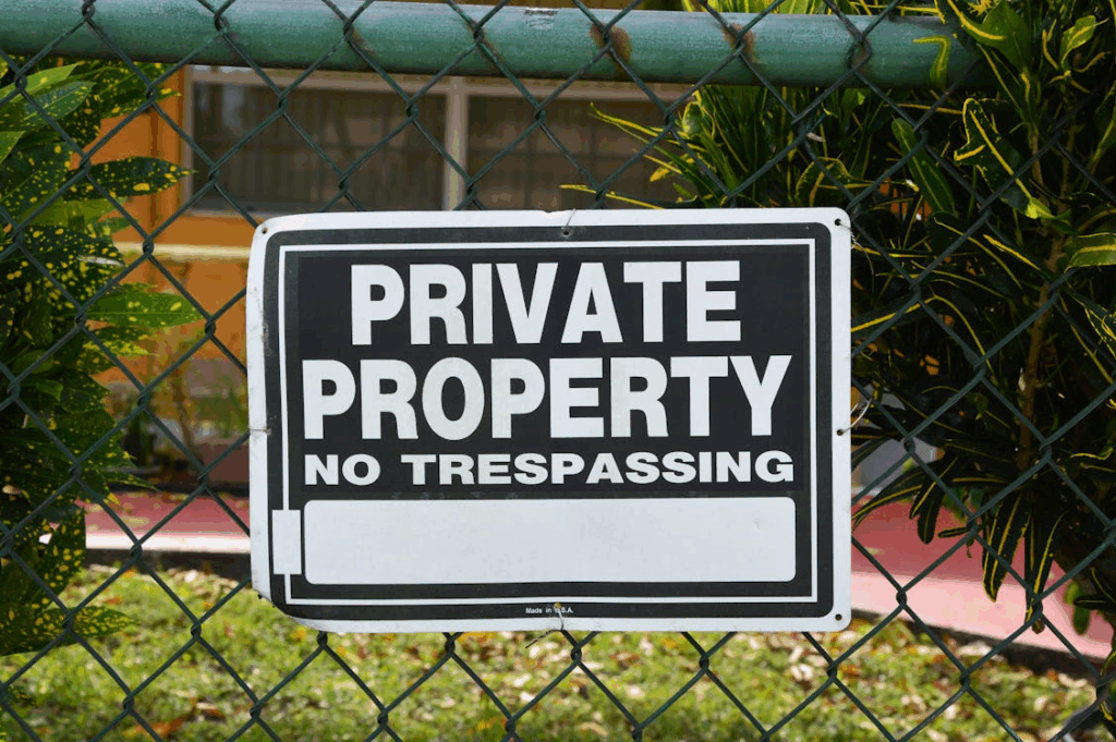Private Property No Trespassing" sign attached to a chain-link fence, representing the legal boundaries homeowners establish to prevent entry by squatters and protect their property rights.