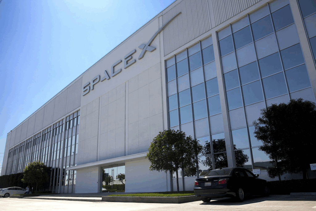 SpaceX Headquarters building in Hawthorne, California. A modern white structure with large glass windows and the SpaceX logo prominently displayed on the facade. This facility represents the company that boosted Google profits by $8 billion through their investment.