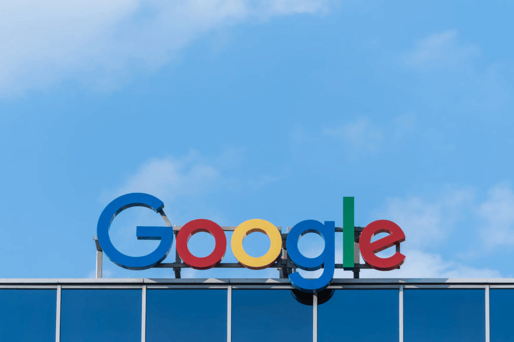 Google logo displayed on top of a building against a clear blue sky. The iconic multicolored Google sign (blue, red, yellow, blue, green, red) is mounted on what appears to be one of the company's office buildings.
