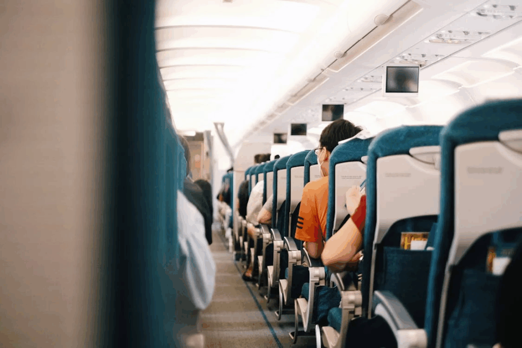 Interior view of an airplane cabin showing multiple rows of blue passenger seats filled with travelers, including plus-sized passengers. The image is taken from an aisle perspective, showing passengers seated throughout the cabin with natural lighting coming through the aircraft windows.