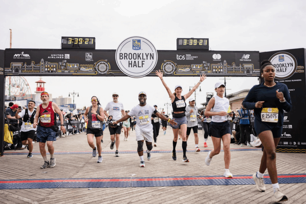Runners crossing the finish line at the Brooklyn Half Marathon with the race clock displaying 3:39:27.