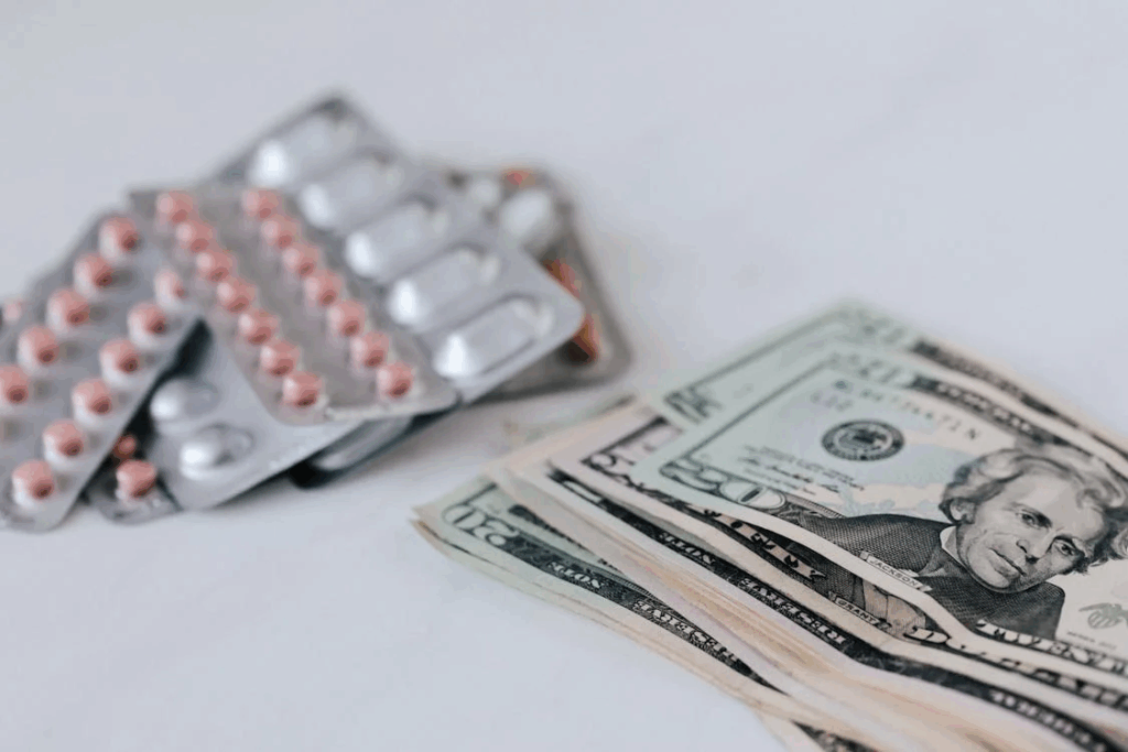 Prescription medication blister packs next to stack of dollar bills, illustrating the high out-of-pocket costs patients face even with insurance coverage.