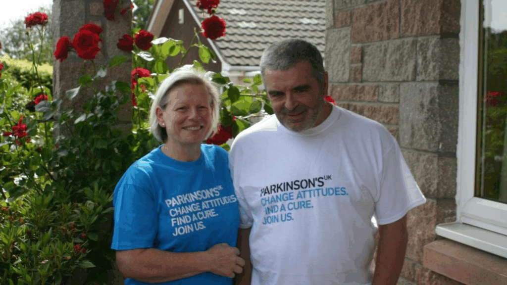Joy and Les Milne wearing Parkinson's UK shirts in their garden. This shows how the woman who smells illness turned her personal promise into hope for millions.