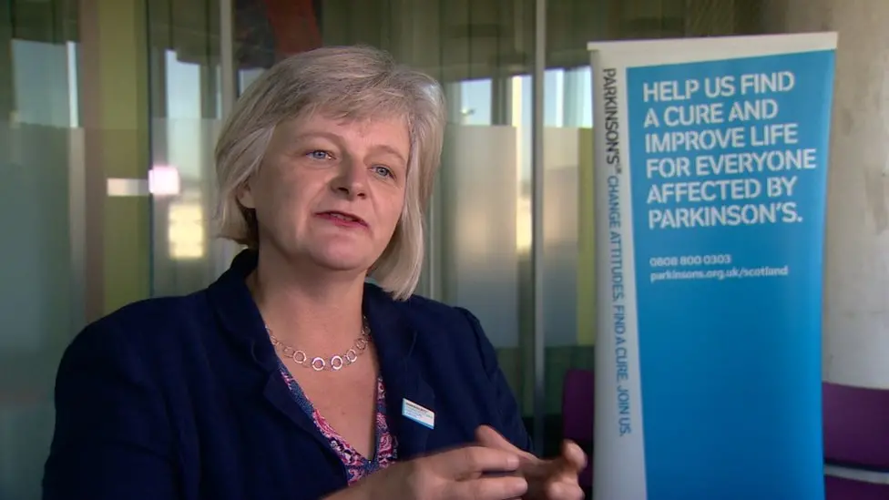  Katherine Crawford speaking next to a Parkinson's UK banner at an event. 