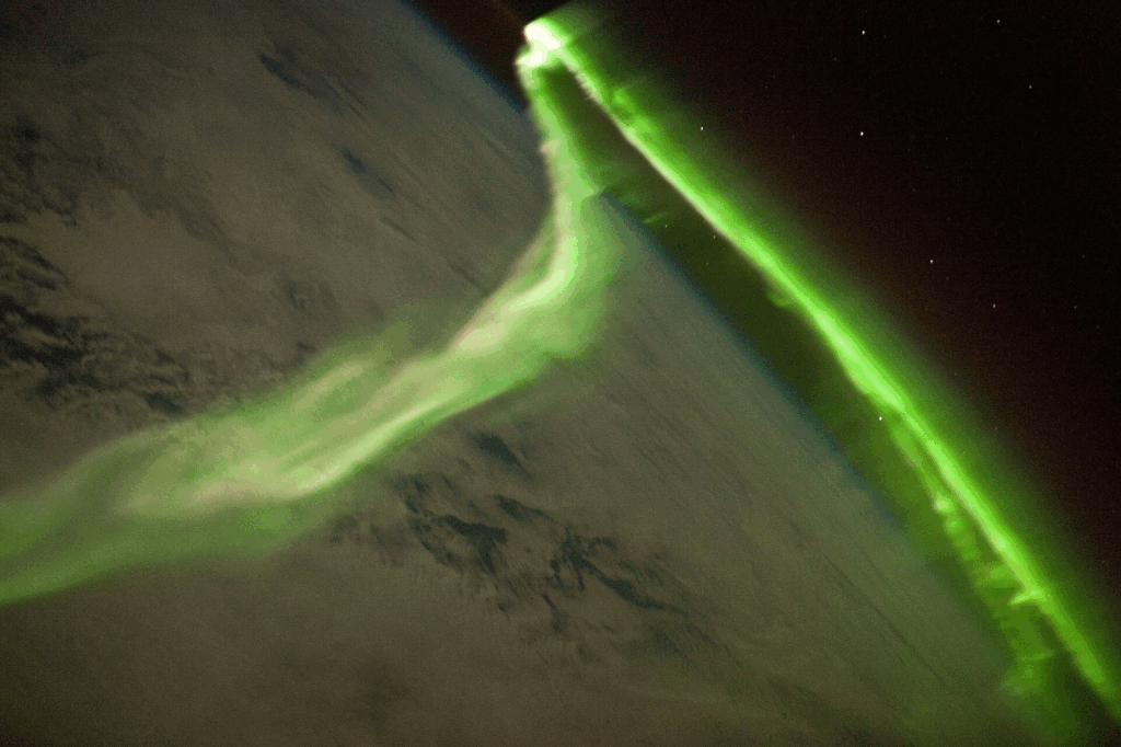 Aurora borealis photographed from space station showing charged particles interacting with Earth's magnetic field.