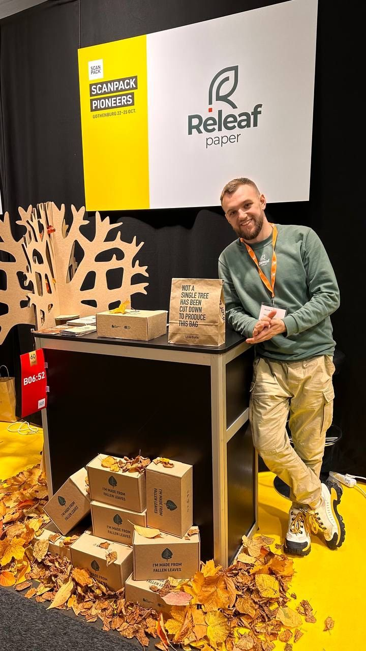 Valentyn Frechka posing at his Releaf Paper stand at a trade show, showing how his company is turning leaves into paper.