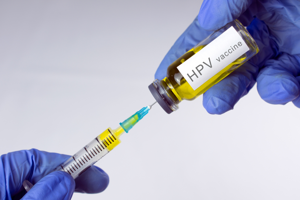 Hands in blue gloves are typing a yellow vaccine in a syringe. HPV vaccination concept. close-up, selective focus