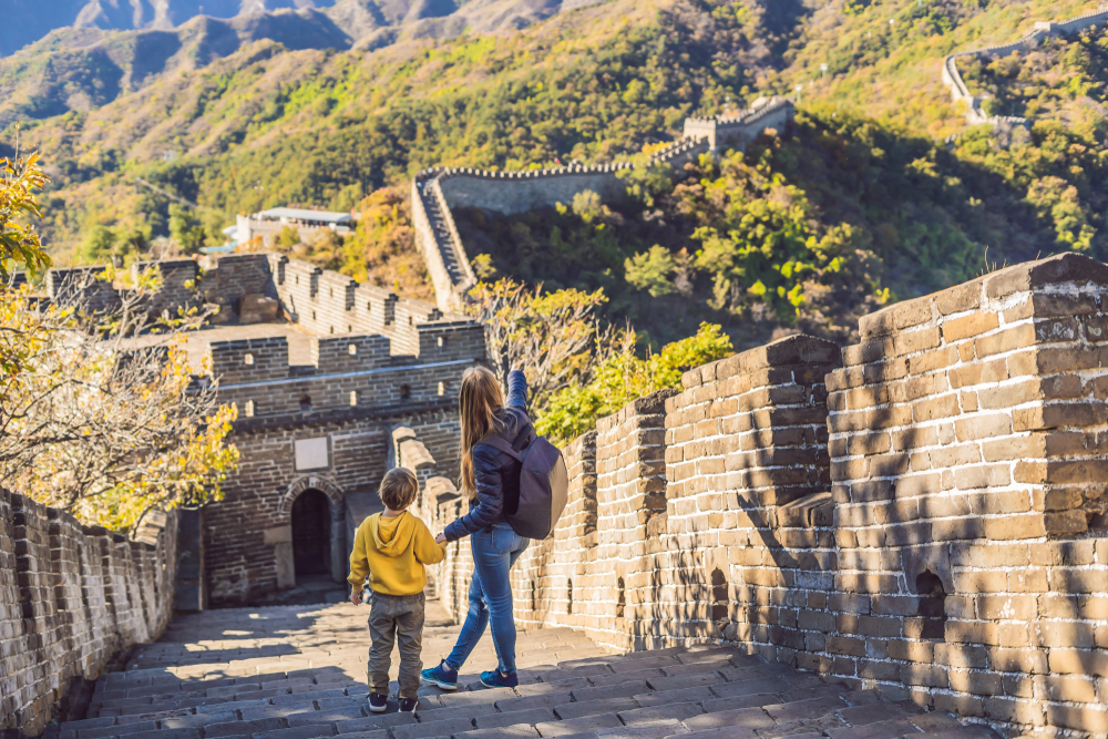 Happy cheerful joyful tourists mom and son at Great Wall of China having fun on travel smiling laughing and dancing during vacation trip in Asia. Chinese destination. Travel with children in China