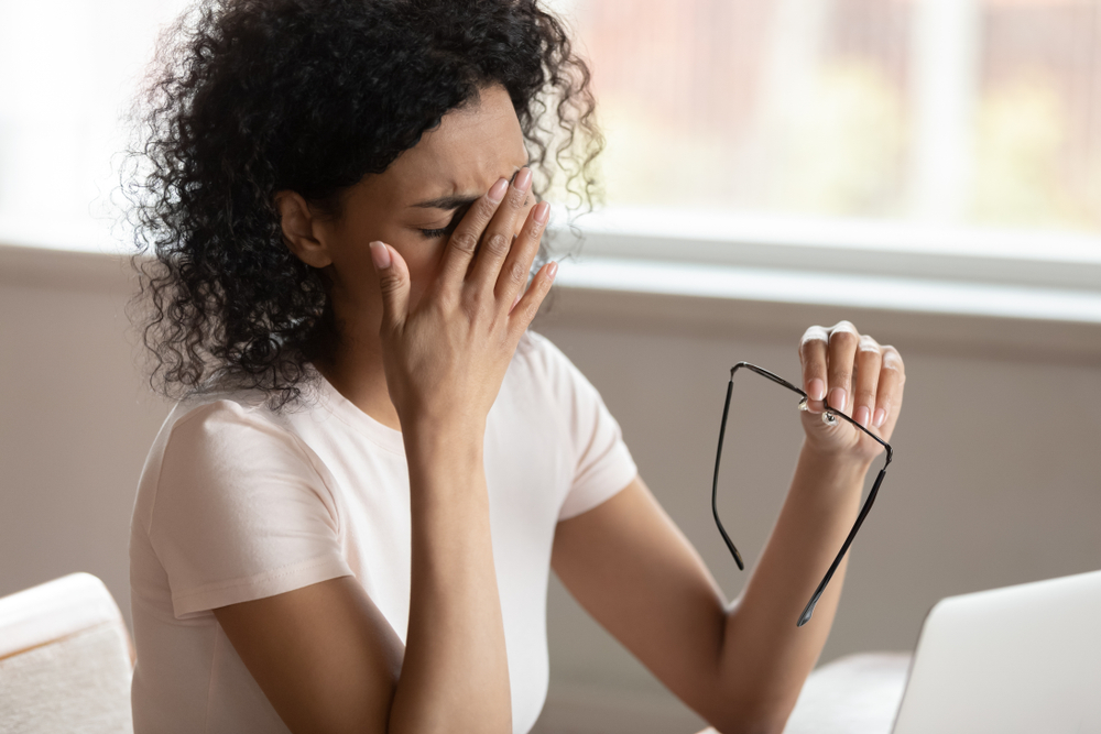 Tired african american millennnial woman dropping eyeglasses, rubbing eyes, feeling exhausted after long working day with computer, suffering from eye strain, blurred vision, dry eyes syndrome.