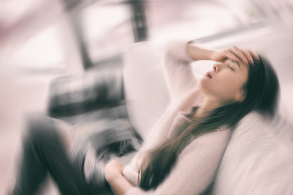 Sick woman with headache feeling faint vertigo holding head in pain with fever and migraine. Blurry motion blur background.