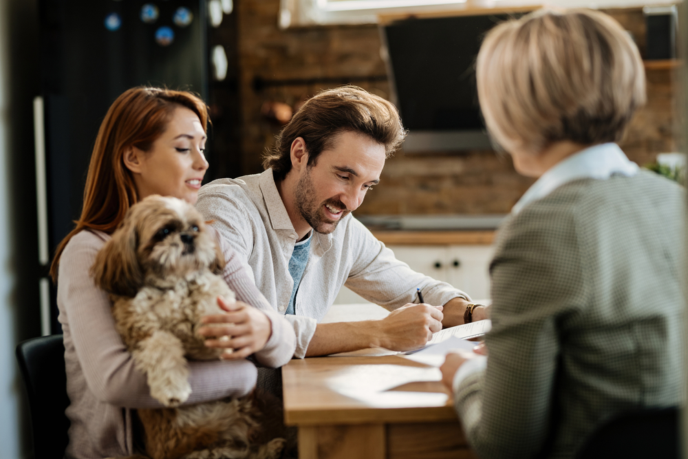 Happy man signing a contract while being with his wife on a meeting with financial advisor.
