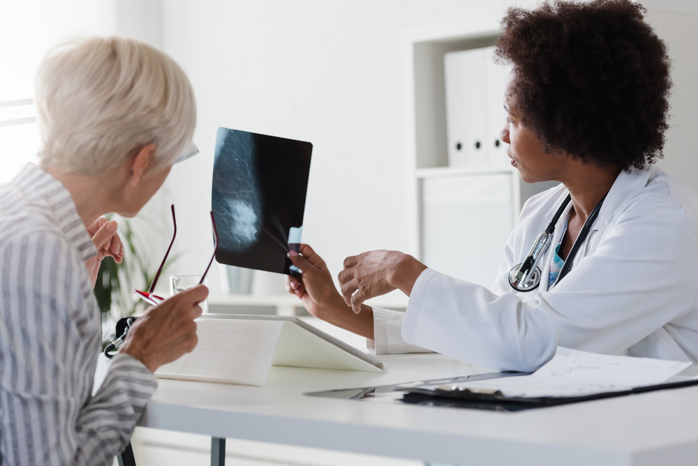 A female doctor sits at her desk and talks to a female patient while looking at her mammogram. Brest cancer prevention
