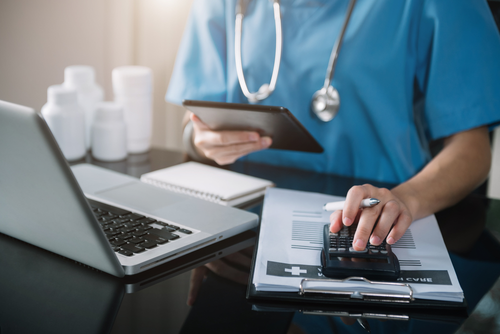 Doctor physician with tablet calculate medical fee costs and revenue. practitioner use calculator at clinic.