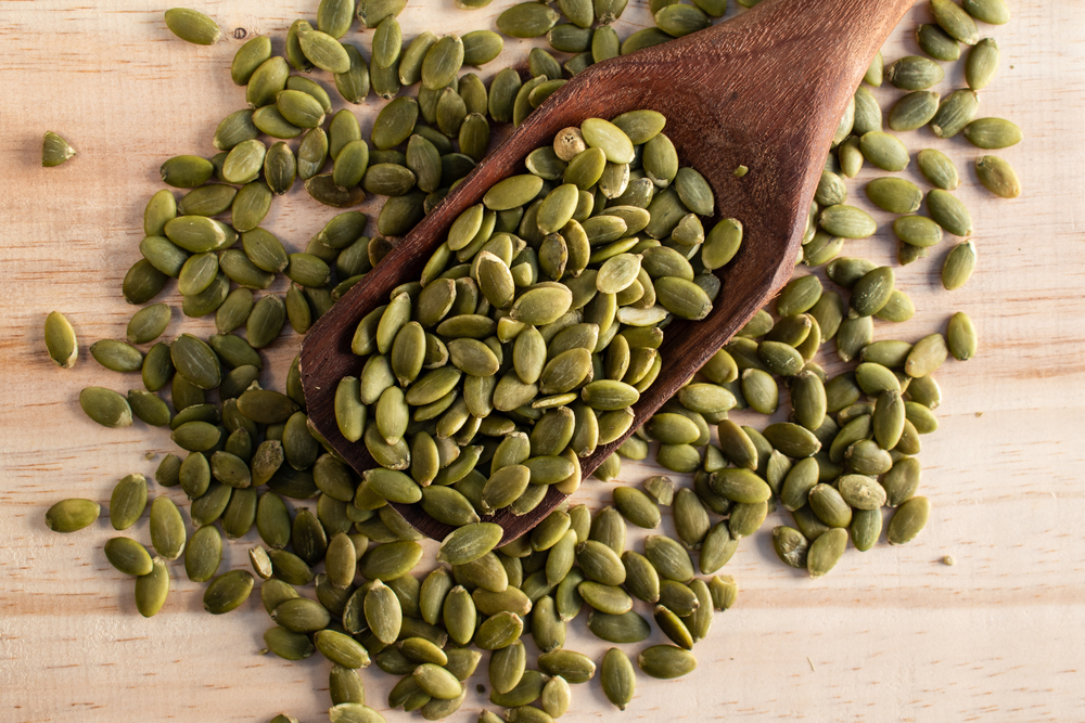 Roasted pumpkin seeds in a wooden spoon on wooden background